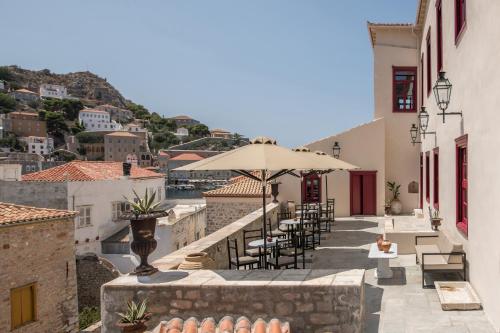 un patio con mesas, sillas y una sombrilla en FOS Hydra residence en Hydra