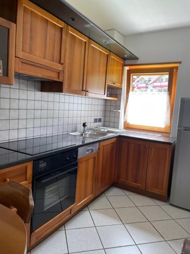 ポッツァ・ディ・ファッサにあるAppartamento Pradelのキッチン(木製キャビネット、シンク、窓付)