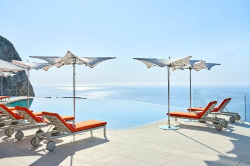 eine Gruppe von Stühlen und Sonnenschirmen neben einem Pool in der Unterkunft The Maybourne Riviera in Roquebrune-Cap-Martin