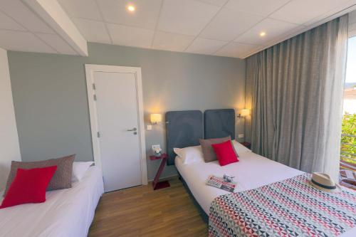 a hotel room with two beds with red pillows at Hôtel Méditerranée in Calvi