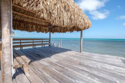 a wooden pier with a straw umbrella and the ocean at Suite 3 at Island Pearl Gold Standard Certified in Caye Caulker