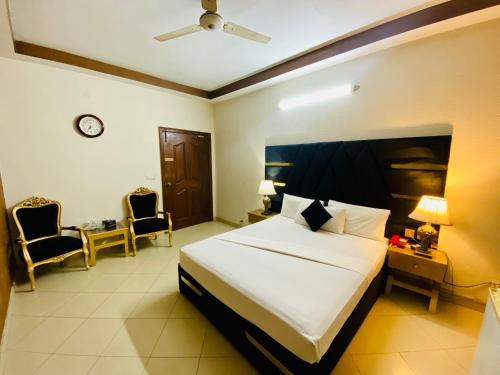 a bedroom with a bed and two chairs and a clock at Fiesta Inn Hotel & Resorts Multan in Multan