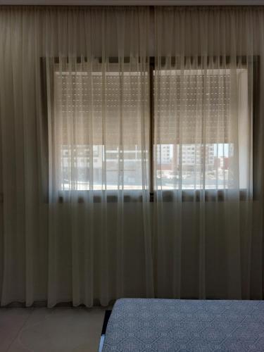 a bedroom with white curtains and a bed and a window at Très bel appart climatisé proche de la plage in Agadir
