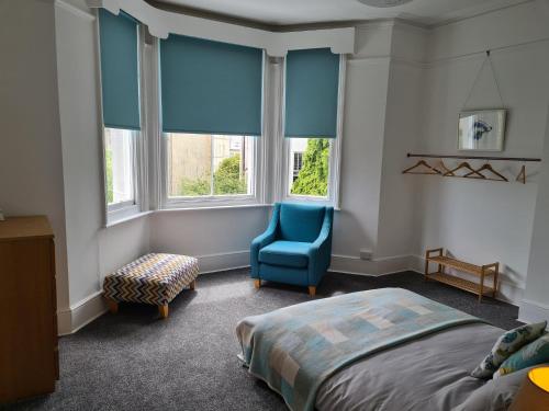a bedroom with a bed and a blue chair and windows at Gorgeous Sea View Apartment 5 mins To The Beach in St. Leonards