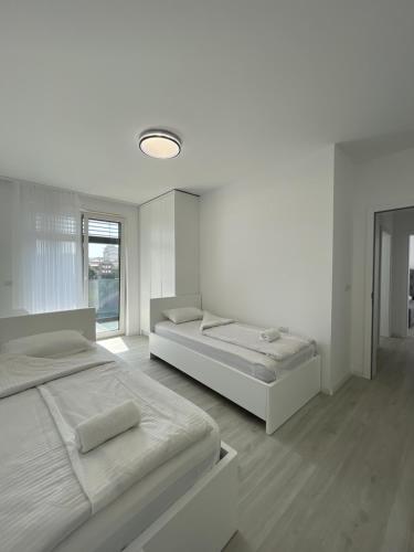 a white bedroom with two beds and a window at Gega Apartments in Gjakove