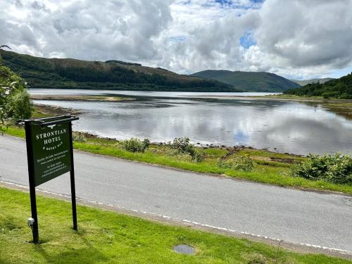 a sign on the side of a road next to a lake at The Strontian Hotel in Strontian
