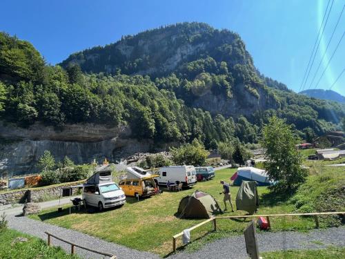 a group of tents and vehicles parked in front of a mountain at Hüttenhotel Husky Lodge in Muotathal
