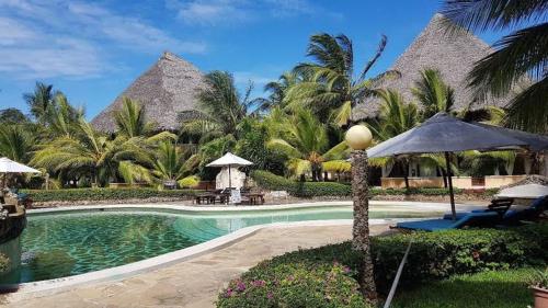 a resort with a swimming pool and palm trees at Tembo Baharini Beach Cottage in Malindi