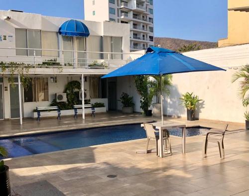 a blue umbrella and a table and chairs next to a pool at Hotel Casa Victoria Rodadero Reservado in Gaira