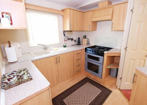 uma cozinha com armários de madeira e um forno com placa de fogão em Hedgehog Holiday Home in the countryside, 10 mins to Lligwy beach em Llandyfrydog