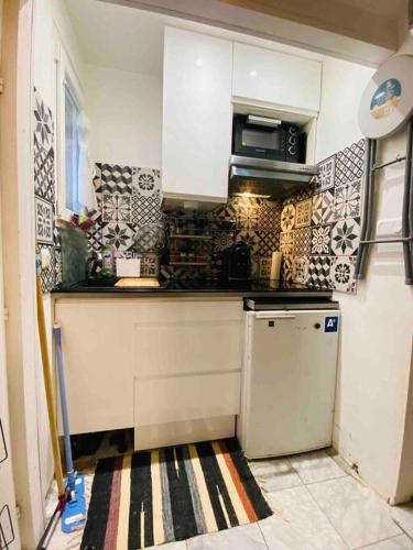 Elle comprend une petite cuisine avec des placards blancs et un réfrigérateur. dans l'établissement Studio - Butte aux cailles 13eme, à Paris