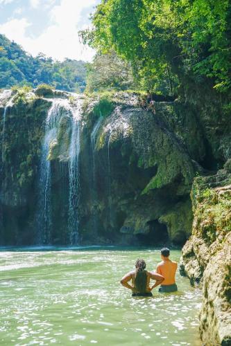 two people sitting in the water in front of a waterfall at El Retiro Lanquin in Lanquín