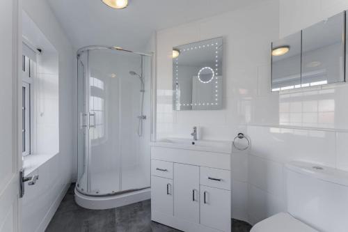een witte badkamer met een douche en een wastafel bij Westward House - Norfolk Cottage Agency in Sheringham