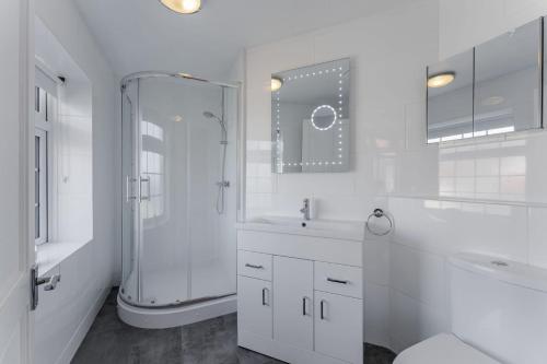 a white bathroom with a shower and a sink at Westward House - Norfolk Cottage Agency in Sheringham