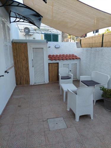 eine Terrasse mit weißen Stühlen, Tischen und einem Sonnenschirm in der Unterkunft CASA DEL SOLE in Ischia