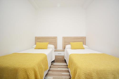 two beds with yellow sheets in a room at Apartamentos de Playa en el centro de O Grove in O Grove