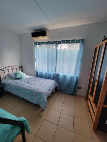 1 dormitorio con 1 cama y una ventana con cortinas azules en Villa Teresita - vista hermosa, en Coco