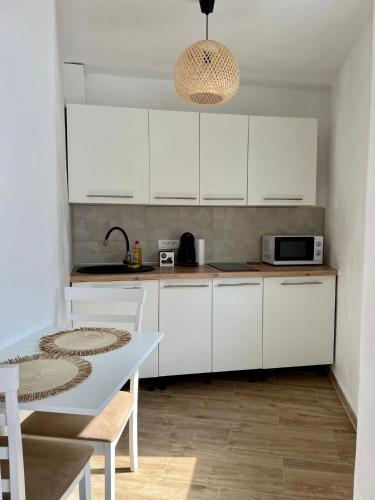 a kitchen with white cabinets and a table and a microwave at Lara Residence in Băile Herculane
