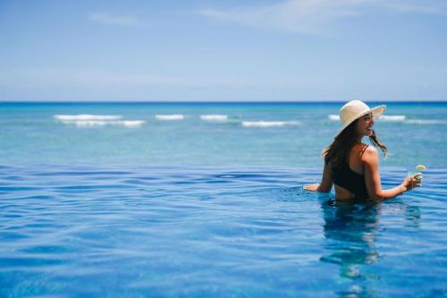 a woman sitting in the ocean holding a drink at Sheraton Waikiki Beach Resort in Honolulu