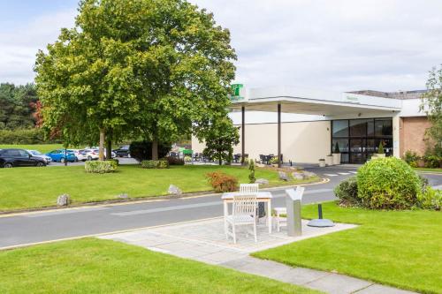 a building with a white bench in front of a road at Holiday Inn Newcastle Gosforth Park by IHG in Newcastle upon Tyne
