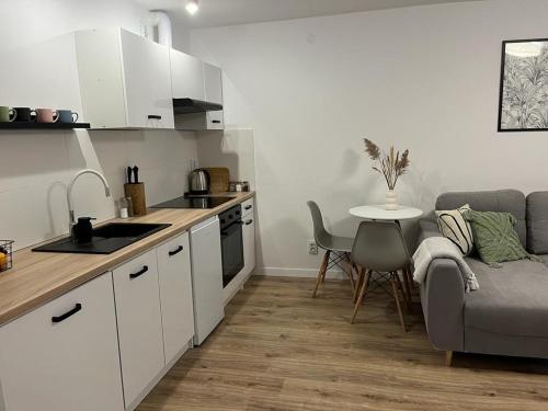 a kitchen with white cabinets and a table and a couch at Apartament Niko Nad Zatoką Pucką in Puck