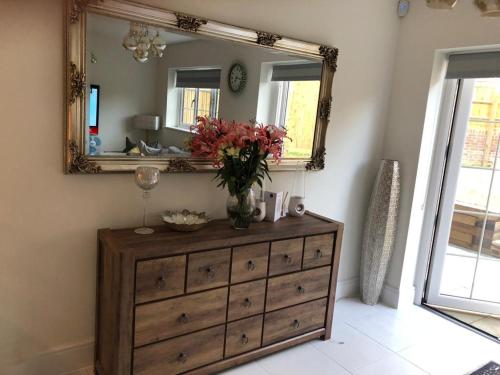 a dresser with a mirror and a vase with flowers on it at Croydon Near London in Shirley