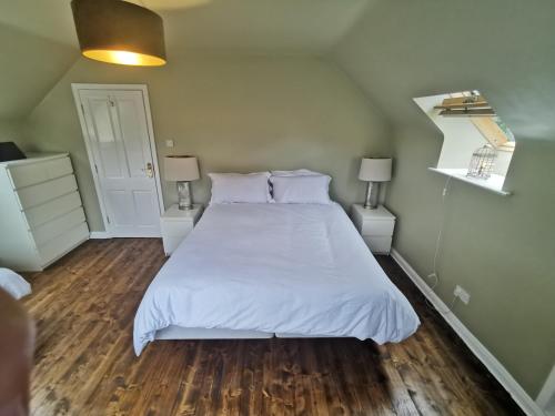 a bedroom with a bed with white sheets and wood floors at Blue Stack View in Edergole Bridge