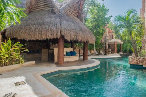 a resort with a swimming pool with a straw hut at Luxury Aldea Zama 2bed - 2bat Apartment Private Terrace & Swim Up in Tulum