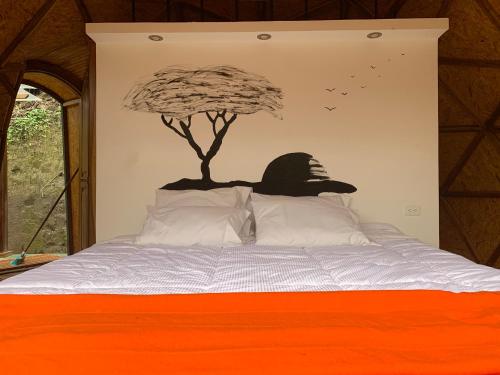 a bed with a tree on the wall at Magic Elf Glamping in Mindo