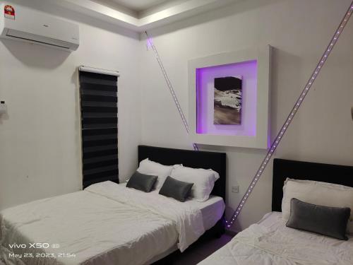 two beds in a bedroom with purple lights on the wall at Santai D villa in Merlimau