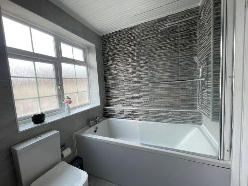 a bathroom with a tub and a toilet and a window at Luxurious Detached Holiday House Free Parking near Airport Town Centre Railway Station in Luton