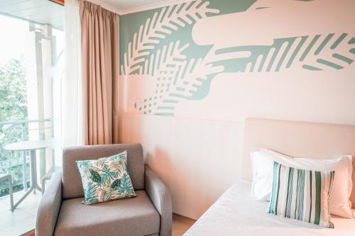 a bedroom with a chair and a wall with a plant mural at Calimera Ralitsa Superior Hotel - Ultra All Inclusive plus Aquapark in Albena