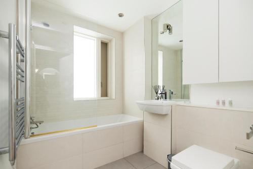 un bagno bianco con vasca e lavandino di The Copenhagen Place - Enchanting 2BDR Flat with Balcony a Londra