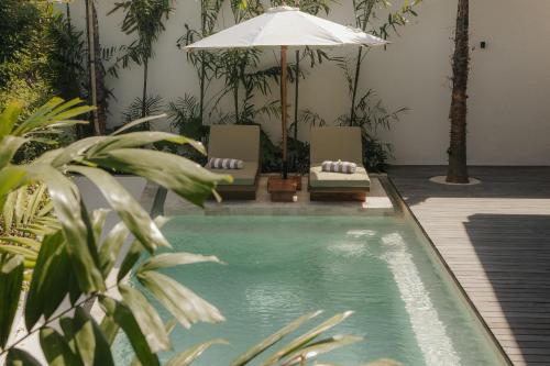 a swimming pool with two chairs and an umbrella at Sage Villas Bingin in Uluwatu