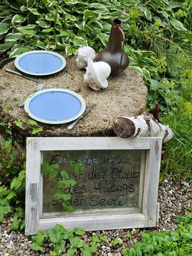 a sign in a garden with plates and a vase at Pension Schatzkisterl in Zwiesel