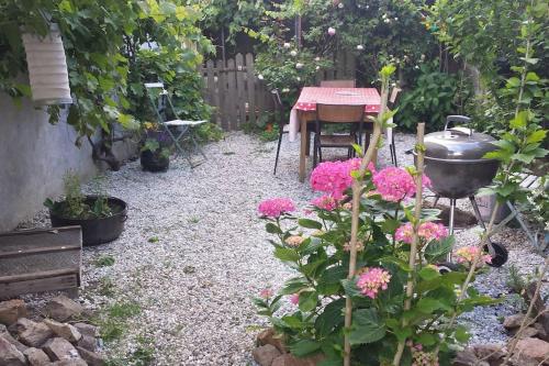 einen Garten mit rosa Blumen, einem Tisch und einem Grill in der Unterkunft Maison avec jardin- Cholet - 20 mn du puy du fou in Cholet