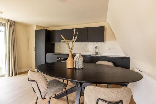 a black dining room table with chairs and a kitchen at VlieMare Appartementen De Kluut in Oost-Vlieland