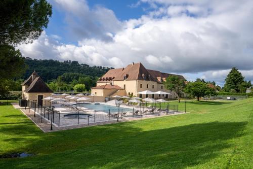 a large building with a swimming pool in front of a yard at Hotel Le Perigord in La Roque-Gageac