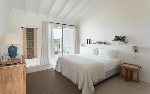 a white bedroom with a bed and a window at Amaria in Aljezur