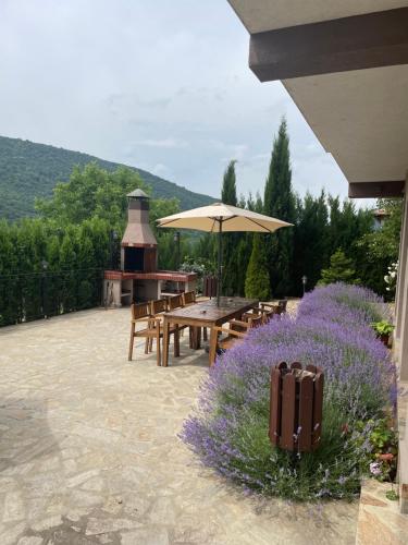 eine Terrasse mit einem Tisch, einem Sonnenschirm und lila Blumen in der Unterkunft Eco House Kitana in Asparuchovo