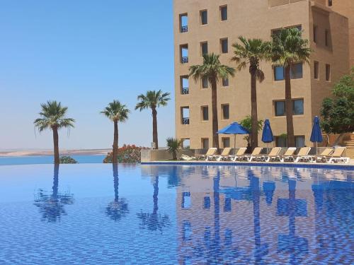 une piscine avec des chaises et des palmiers en face d'un hôtel dans l'établissement Sunset apartment in Samarah Dead Sea resort, à Sowayma