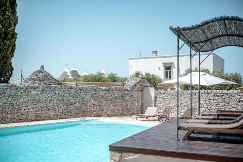 a swimming pool with chairs and a stone wall at Masseria Pavone in Martina Franca