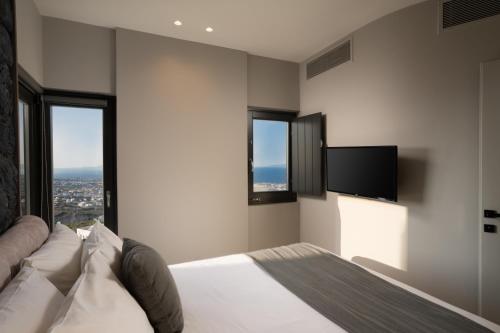 a bedroom with a bed with a television and windows at Apikia Santorini in Pirgos
