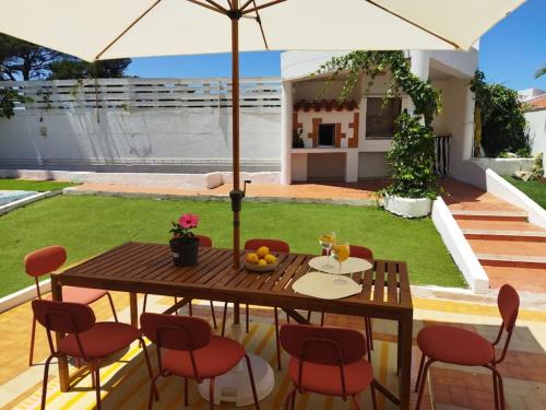 a wooden table with chairs and an umbrella in a yard at Casa Capuchos. Close to Lisbon with Ocean View in Caparica