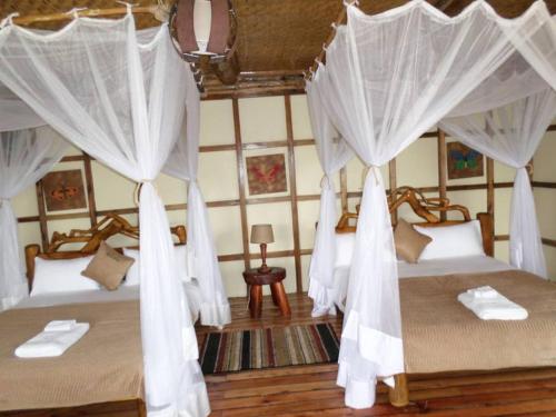 two beds in a room with white curtains at Buhoma Community Haven lodge 