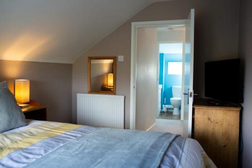 a bedroom with a bed and a television and a bathroom at Baytree Cottage Framlingham in Framlingham