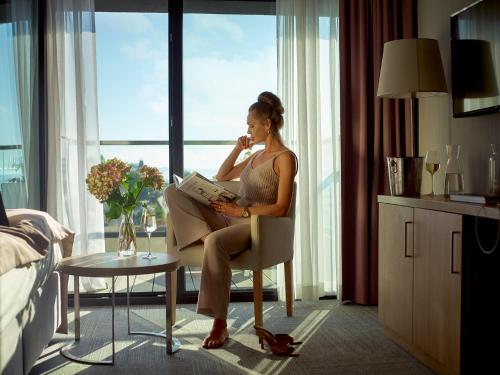 une femme assise sur une chaise en lisant un livre dans l'établissement Baltivia Sea Resort, à Mielno