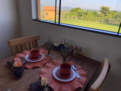a table with two plates and cups and a window at Pousada Pôr do Sol in São João Batista do Glória