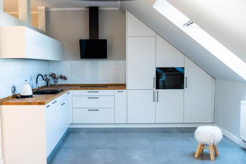 an attic kitchen with white cabinets and a stool at Apartamenty Wielbarska in Szczytno