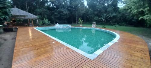 a swimming pool with a wooden deck next to a yard at Bali Suites Itamambuca in Ubatuba